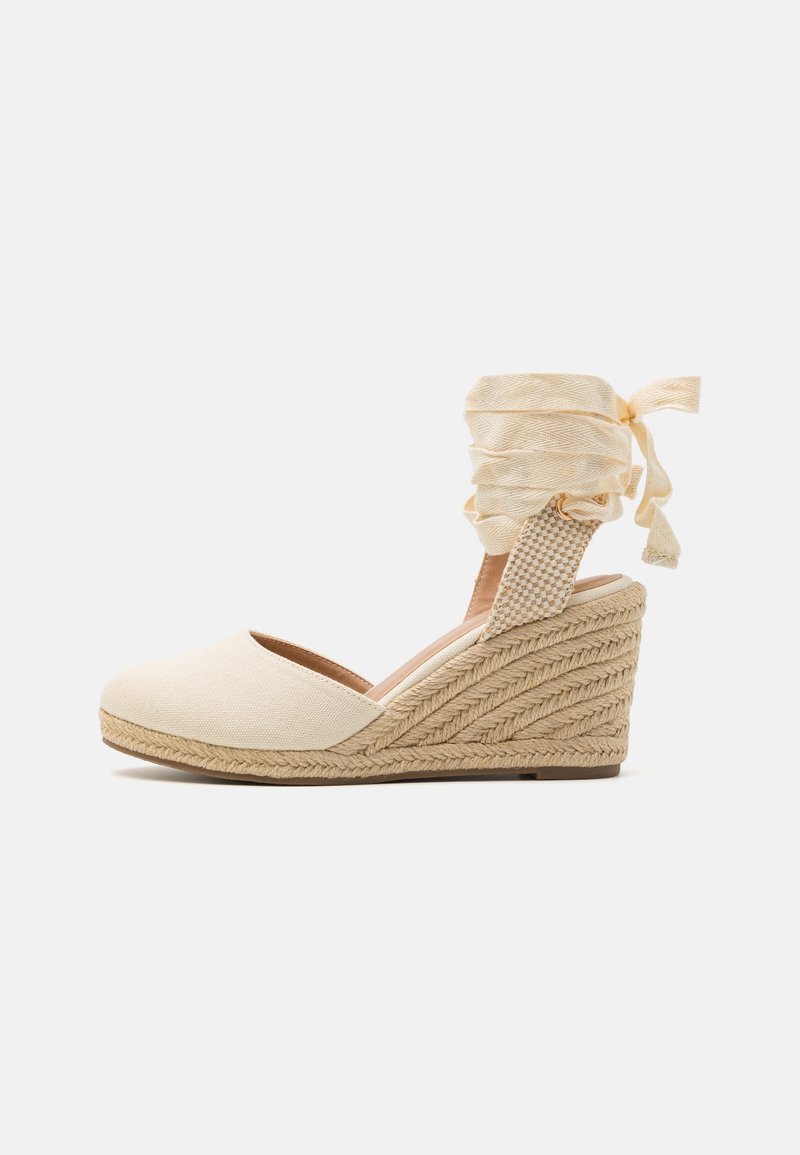 Espadrille compensée en toile beige avec talon en jute tressée et lien à nouer autour de la cheville sur un fond clair uni.