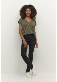 Olive green v-neck t-shirt paired with black skinny jeans and white sneakers. The shirt has short sleeves and a relaxed fit.