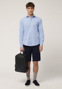 Light blue button-up shirt with long sleeves, navy shorts, black leather backpack, gray socks, and dark shoes. Simple and clean design.