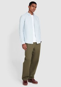 Lichtblauw en wit gestreept overhemd, gedragen over een wit t-shirt, gecombineerd met olijfgroen broek en bruine boot schoenen.