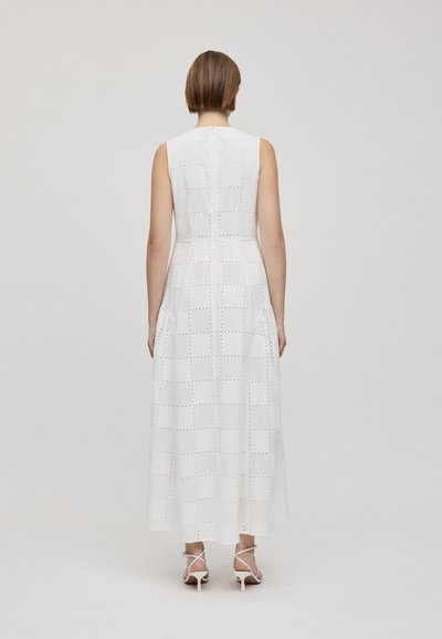 Abito maxi bianco senza maniche con motivo a griglia, caratterizzato da dettagli ritagliati. Tessuto leggero con una silhouette fluida, abbinato a tacchi a strati.
