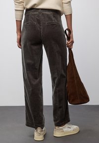 Pantaloni larghi in corduroy grigio con finitura testurizzata, dotati di tasche a toppa; abbinati a una borsa a tracolla in suede marrone e scarpe da ginnastica di tonalità chiara.