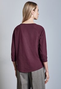 Maronin pitkähihaine paita, jossa on pyöreä kaula-aukko ja kolmanneksen pituiset hihat. Suuntunut kangas, rento malli, yhdistetty ruudullisiin housuihin.