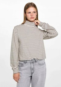 Raidallinen pusero, vaalean beige mustilla raidoilla. Ominaisuuksia pitkät hihat ja rento istuvuus. Yhdistetty vaaleanharmaisiin farkkuihin.