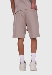 Beige bomulds shorts med sidelommer, syede kanter og en afslappet pasform, parret med hvide strømper og sneakers. Baggrunden er ensfarvet.