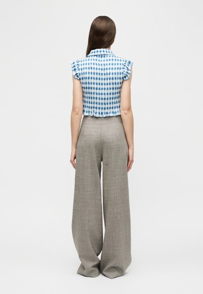 Γυναίκα με ίσια καστανά μαλλιά, που φοράει μπλούζα με κοντά μανίκια και καρώ μπλε και άσπρο μοτίβο και μπεζ παντελόνι ψηλόμεσο, φαρδύ, κοιτώντας προς τα πίσω.