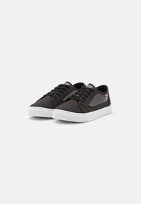 Sorte lærersneakers med hvite gummisåler og runde lisser; har blanke detaljer og en logo på siden. Glatt tekstur, lavprofildesign.
