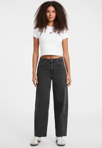 Jeans neri a gamba larga con tasche frontali, vita alta e dettagli cuciti, abbinati a una maglietta bianca corta con una grafica a stella.