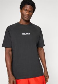 Čierne tričko s krátkym rukávom a okrúhlym výstrihom, s bielym logom "5.10" na hrudi, vyrobené z mäkkej tkaniny s hladkým povrchom.