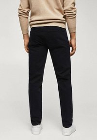 Jean foncé avec une coupe droite, en coton, présentant des coutures minimales et deux poches arrière. Porté avec des baskets blanches.