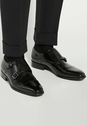 Black leather dress shoes with two silver buckle accents, pointed toe design, and a smooth texture, paired with black dress trousers.