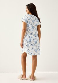 Kortærmet kjole i hvid bomuld med blå blomster mønstre, knælængde, med en afrundet kant og løs pasform, parret med fuzzy beige tøfler.