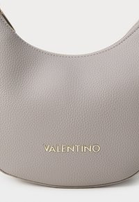 Grå skinnveske med en jevn, teksturert overflate. Har en buet form og gull "VALENTINO"-logo på forsiden. Lukkemekanisme ikke synlig.