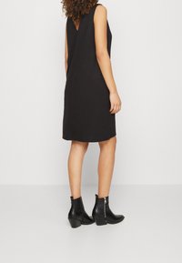 Vestido negro sin mangas con un escote en forma de V en la espalda, combinado con botas negras hasta el tobillo con detalle de cremallera y tacón cónico. Textura de tela suave.
