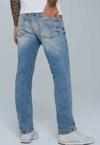 Jeans de color azul claro con corte slim, que presentan bolsillos traseros con costura curva, textura desgastada y costuras de contraste a lo largo de las costuras.