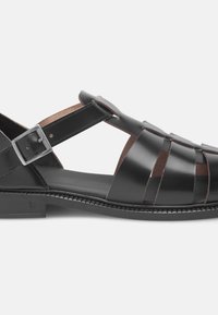 Sandalo nero in pelle con fettucce incrociate, chiusura con fibbia e suola piatta nera con dettagli di cucitura delicati.