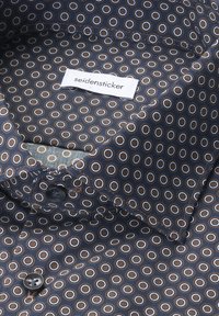 Marineblauw shirtinterieur met een cirkelpatroon in bruin en wit. Het label zegt "seidensticker." Zachte stof met een gladde textuur.