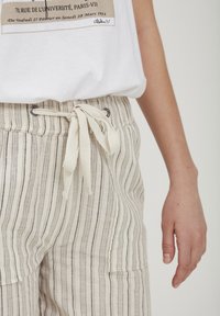 Pantalons légers à rayures avec taille élastique, présentant des lignes verticales beiges et grises, et un design de poche latérale.