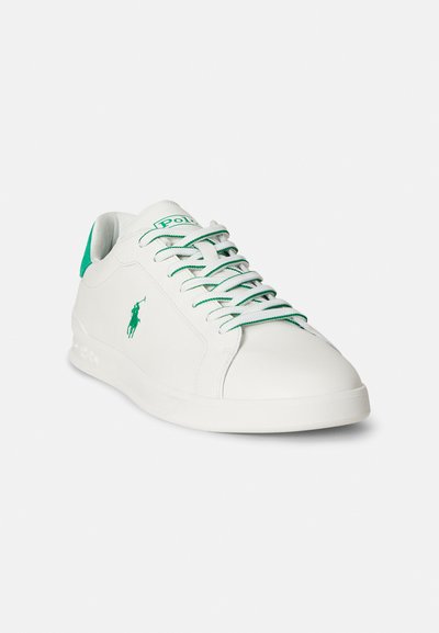 Biały skórzany sneaker z zielonymi akcentami, okrągły nosek, przednie sznurowanie i logo po boku. Gładka faktura z płaską podeszwą.