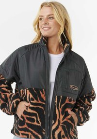Chaqueta de forro polar con un estampado negro y naranja, con cremallera; presenta un bolsillo en el pecho y puños elásticos, combinando materiales suaves y texturizados.
