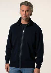 Námornícky zip-up kardigán vyrobený z mäkkej tkaniny, s vysokým golierom, prednou vreckom a rebrovanými manžetami a lemom. Klasický a všestranný dizajn.