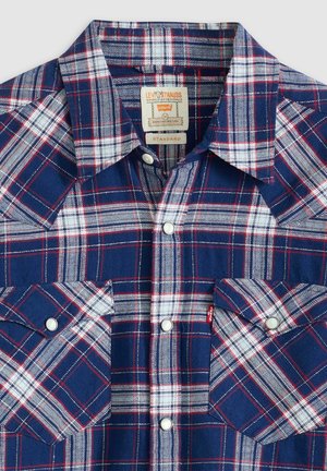 Rutig skjorta med knäppning i marinblått, vitt och rött. Har spetsig krage, två bröstfickor och silverfärgade tryckknappar. Strukturerad tyg.