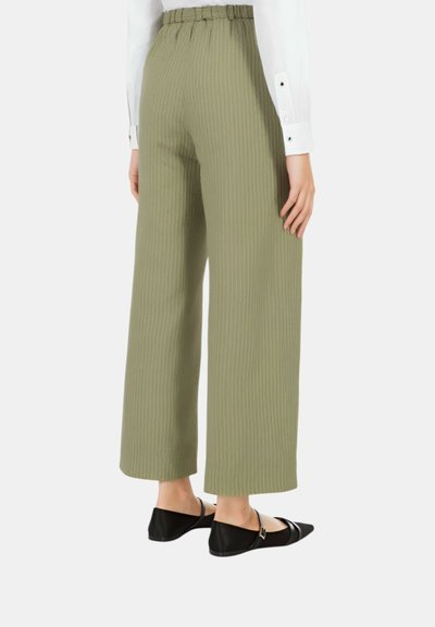 Pantaloni larghi di un verde oliva chiaro con strisce verticali, vita elastica e abbinati a ballerine nere. Texture liscia, vestibilità rilassata.
