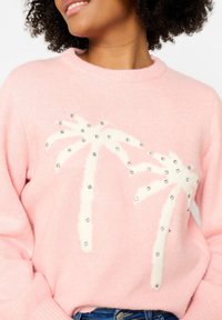 Pull rose en tissu doux avec un motif de palmier blanc orné de strass, col rond et manches longues.