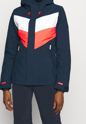 Marineblauw jack met wit en rood chevronpatroon, ritssluiting aan de voorkant, met rits afsluitbare zijzakken, verstelbare manchetten, gedragen met bijpassende marineblauwe broek.