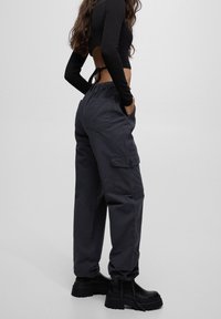 Pantalon cargo gris foncé à coupe décontractée, doté de poches latérales et d'une taille élastique. Associé à des bottines noires épaisses.