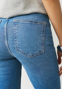 Středně modré džínové kalhoty z denimu s zadní kapsou a kontrastním šitím, s přiléhavým střihem a hladkou texturou.