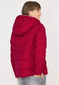 Rød pufferjakke med hætte, med chevron-quilting og ribbede manchetter. Materialet ser blødt og struktureret ud med sidelommer.