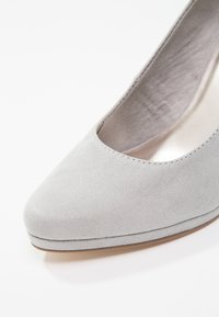Escarpin à talon haut en daim gris clair avec bout pointu et doublure intérieure lisse. Présente une couture discrète le long du bord.