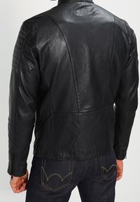 Black leather motorcycle jacket with a quilted shoulder design, fitted shape, and zippered cuffs, paired with blue denim jeans.