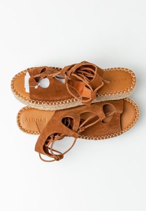 Brune ruskindssandaler med snørebånd, syninger langs kanterne og jutesåler med espadrille-stil, prydet med "ALOHA" indpræget på den lyse læderindersål.