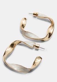 Guldfarvede metal hoops med en bølget design og hvide iriserende accenter. Øreringene har en stift bagkonstruktion for sikker bæring.