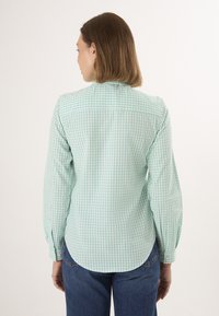 Chemise à manches longues à carreaux verts et blancs avec un ourlet arrondi. Fabriquée en coton tissé avec une texture douce. Design de col simple.