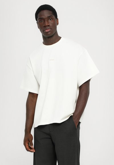 T-shirt bianco oversize a maniche corte realizzato in cotone morbido, con un discreto logo "WON" in beige. Completa i pantaloni scuri indossati.