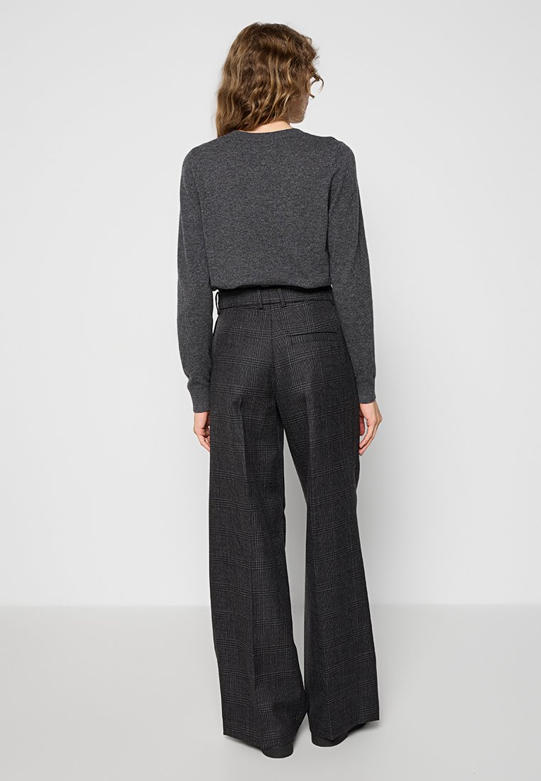 Donkergrijs, lange mouwen top gecombineerd met brede, geruite broek in zwart en grijs. De broek heeft een hoge taille en achterzakdetails.