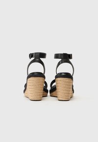 Black leather wedge sandals with braided jute heels, featuring ankle straps and an open toe design. Textured materials and sturdy construction.