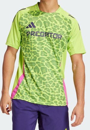 Homme portant un t-shirt de sport Adidas Predator vert à imprimé léopard avec des panneaux latéraux roses et un short violet, posant avec les bras détendus.