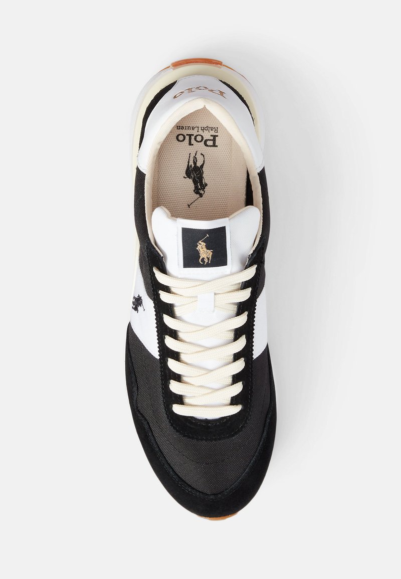 Chaussure de sport noir et blanc avec un dessus en tissu texturé, des lacets crème et une semelle en caoutchouc beige. Présente une étiquette logo sur la languette.