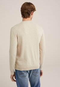 Suéter de punto beige con mangas largas y cuello redondo, que presenta una textura suave y un dobladillo acanalado. Lleva puesto sobre unos jeans de mezclilla azul.