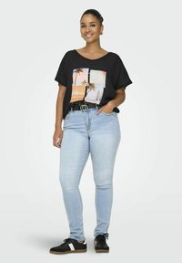 Camiseta negra de gran tamaño con gráfico colorido de una escena de playa, jeans ajustados de color azul claro, zapatillas negras con detalles blancos, cinturón delgado.