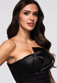 Abito nero senza spalline in raso con corpetto strutturato, dettaglio a fiocco e pieghe strutturate lungo la vita. Finitura liscia e lucida.