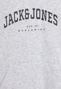 Felpa grigia con finitura testurizzata. Presenta una stampa nera prominente: "JACK&JONES", "EST. 90" e "WORLDWIDE". Include una tasca a marsupio.
