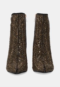 Botines negros con adornos dorados brillantes, que presentan un diseño alto y esbelto y un cierre de cremallera en el lateral.