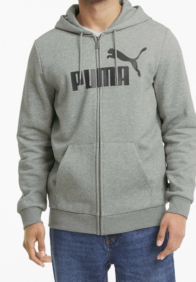 Felpa con zip grigia realizzata in tessuto morbido. Presenta un grande logo nero di Puma sul petto, tasche frontali e cappuccio con cordino regolabile.