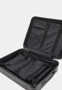 Valigia rigida nera con apertura con zip, dotata di un interno decorato e più scomparti con zip e cinghie per l'organizzazione.