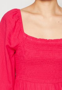 Růžové dlouhé šaty s obdélníkovým dekoltem, nařaseným živůtkem a splývavou sukní. Vyrobeny z lehké látky s texturovaným povrchem.